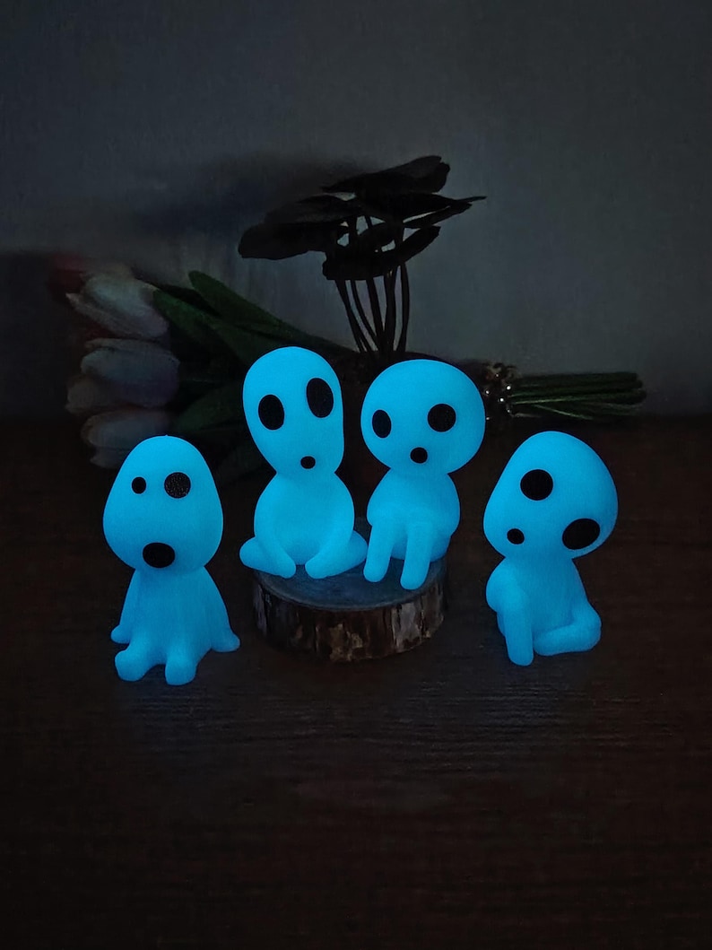 May include: Four blue glowing figurines with round eyes and mouths, sitting on a wooden surface. The figurines are reminiscent of the characters from the animated film "My Neighbor Totoro".