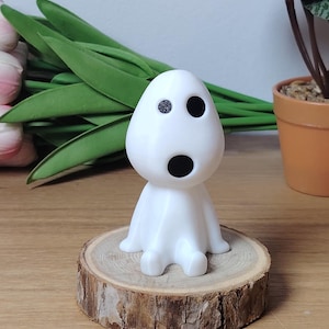 K&ouml;nnte beinhalten: Wei&szlig;e 3D-gedruckte Figur eines Charakters mit einem runden Kopf, zwei schwarzen Augen und einem schwarzen Mund. Die Figur sitzt auf einer Holzscheibe.