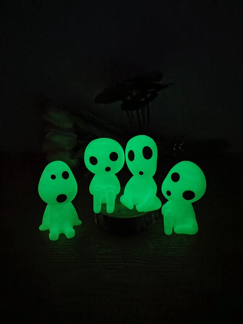 May include: Four glowing green figurines with round eyes and mouths. The figurines are sitting on a wooden surface.
