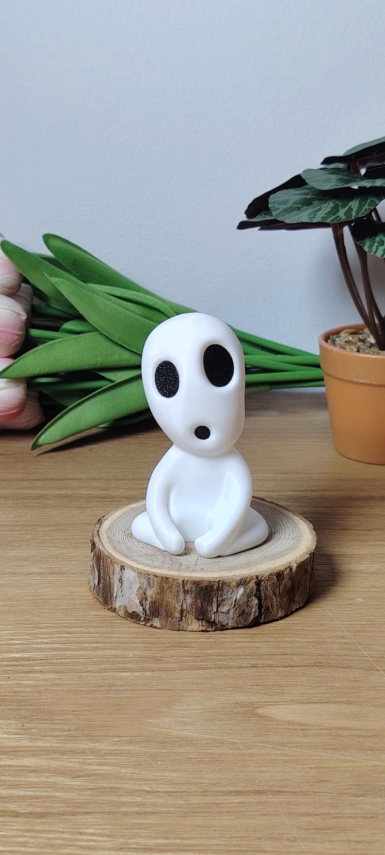 K&ouml;nnte beinhalten: Wei&szlig;e Figur eines Charakters mit gro&szlig;en Augen und einem &uuml;berraschten Ausdruck, der auf einem Holzscheit sitzt.