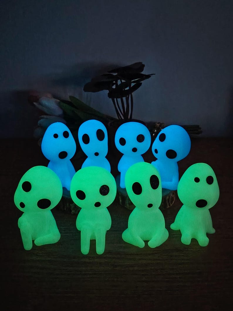 May include: A group of eight glow-in-the-dark figurines. The figurines are shaped like small, round people with large eyes and simple features. They are in two colors: blue and green.