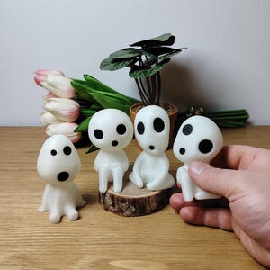 May include: Four white, glowing, spirit-like figures with black eyes. Three of the figures are sitting on a wooden log, while the fourth figure is being held in a hand.