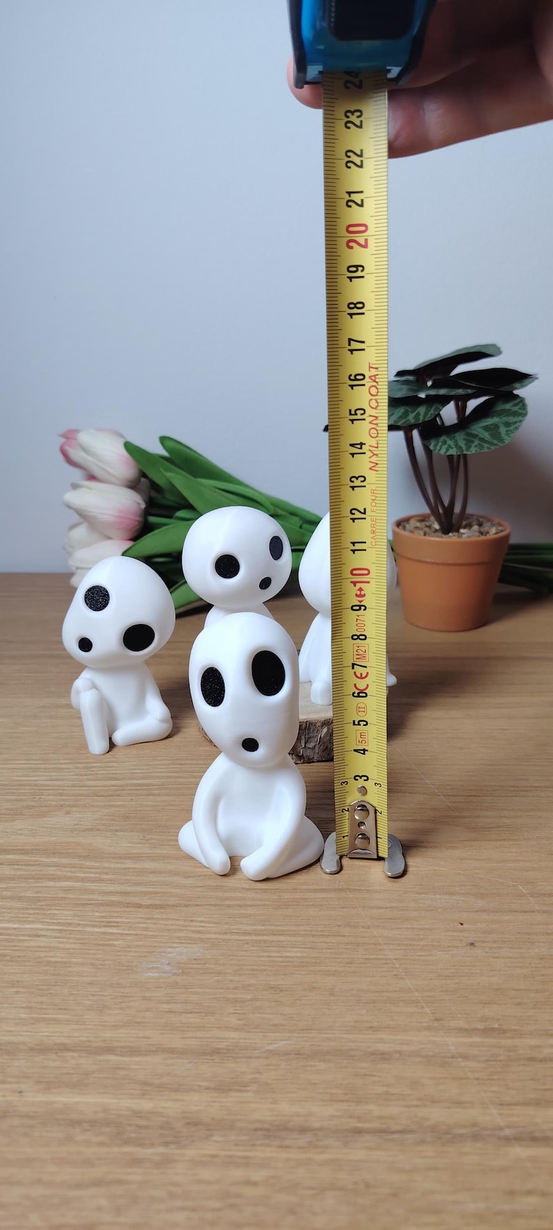K&ouml;nnte beinhalten: Vier wei&szlig;e Figuren mit schwarzen Augen und M&uuml;ndern, die an Figuren aus dem Animationsfilm "Mein Nachbar Totoro" erinnern. Die Figuren sitzen auf einer Holzoberfl&auml;che, im Hintergrund befindet sich ein Ma&szlig;band.