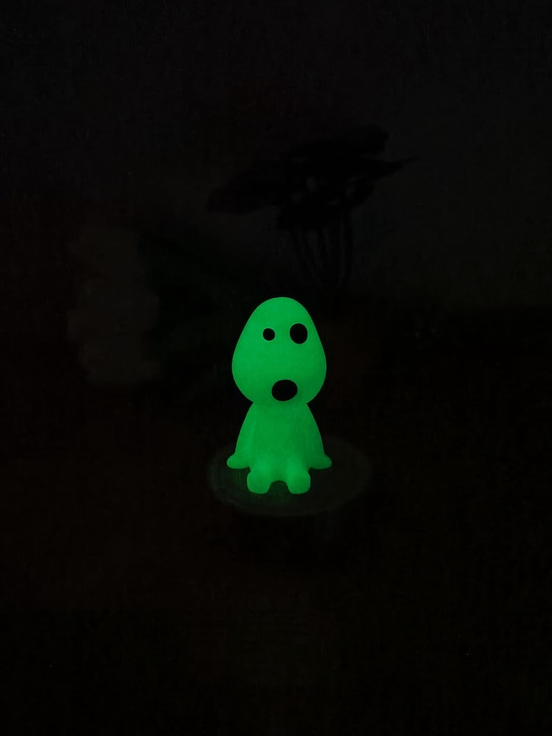 May include: A green glow-in-the-dark figurine of a ghost with two eyes and a mouth. The ghost is sitting on a small white base.