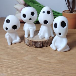 K&ouml;nnte beinhalten: Vier wei&szlig;e Figuren mit schwarzen Augen und M&uuml;ndern, die an Figuren aus dem Animationsfilm 'Mein Nachbar Totoro' erinnern. Die Figuren sitzen auf einer Holzscheibe.