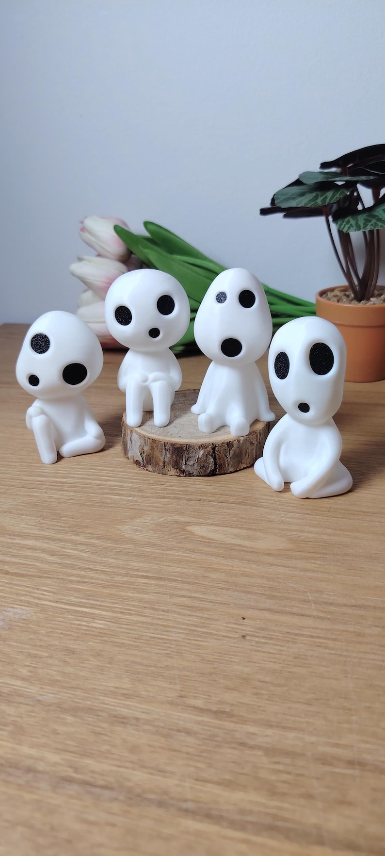 K&ouml;nnte beinhalten: Vier wei&szlig;e Figuren mit schwarzen Augen und M&uuml;ndern, die an Figuren aus dem Animationsfilm 'Mein Nachbar Totoro' erinnern. Die Figuren sitzen auf einer Holzscheibe.
