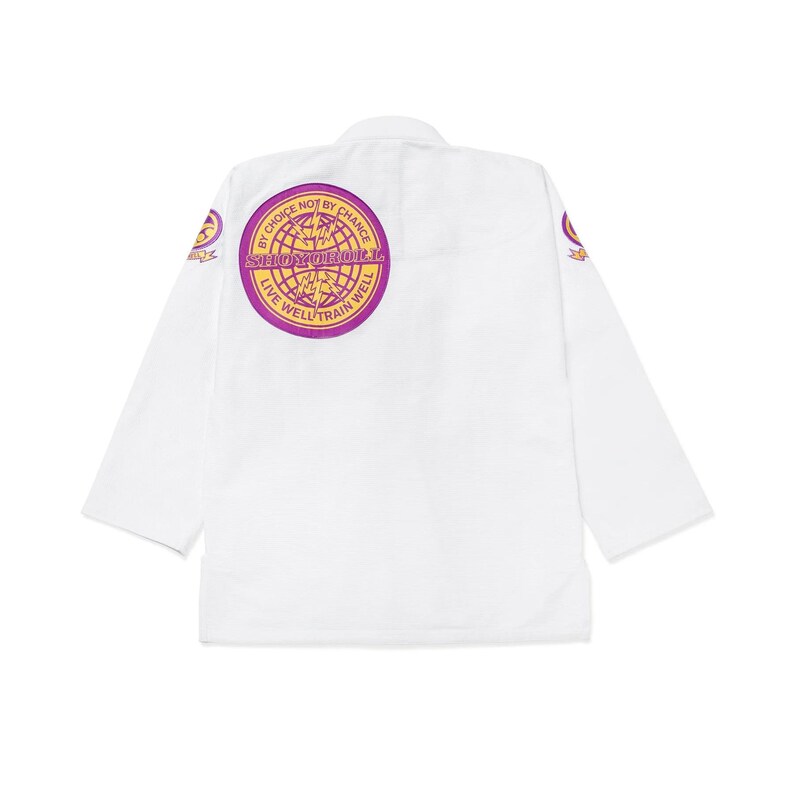 Puede incluir: Uniforme blanco de artes marciales con mangas largas. La espalda presenta un emblema circular con el texto "By Choice Not By Chance" y "Live Well Train Well" en morado y dorado. Emblemas adicionales en las mangas.