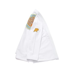 Peut inclure: Kimono de sport blanc plié. Le kimono présente un écusson avec le texte "ALBA COMPETITION" et un logo orange, jaune et bleu. Un logo "A" doré est également visible.