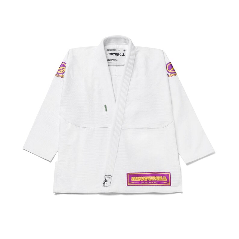 Puede incluir: Uniforme blanco de artes marciales con la marca "SHOYOROLL" en un parche rectangular morado y dorado. El uniforme tiene parches morados y dorados en las mangas. El uniforme est&aacute; hecho de una tela duradera.