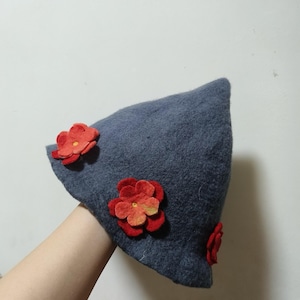 May include: A gray felt hat with red felt flowers attached to the side. The hat is shaped like a cone.