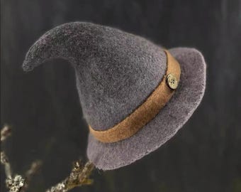 May include: A gray witch hat with a curved tip, featuring a brown band and a button. The hat is made of felt and has a wide brim. The hat is a Halloween costume accessory.