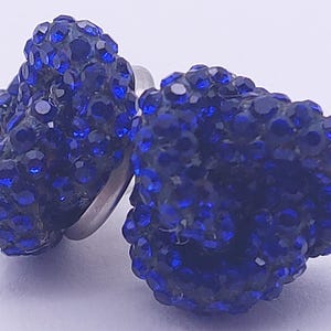 Könnte beinhalten: Ein Paar blaue Kristall-Ohrstecker. Jeder Ohrring hat eine Ansammlung kleiner, facettierter blauer Kristalle, die einen funkelnden Effekt erzeugen. Die Ohrringe haben einen silberfarbenen Stecker.