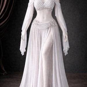 Könnte beinhalten: Ein weißes, fließendes Kleid mit geteiltem Rock und schulterfreien Ärmeln. Das Oberteil und die Taille sind mit funkelnden Strasssteinen verziert. Das Kleid wird auf einer Schaufensterpuppe präsentiert, die sein elegantes Design und seinen zarten Stoff zeigt.