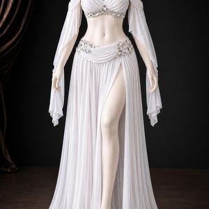 May include: A white two-piece outfit consisting of a halter-style crop top and a floor-length skirt. The top features pleated fabric, off-the-shoulder sleeves, and silver-toned embellishments. The skirt has a high waist, side slit, and pleats.