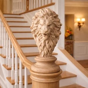 May include: A carved wooden lion head sculpture atop a stair railing post. The lion has a detailed mane and open mouth. The staircase has white risers and light wood treads and handrails.