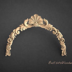 May include: A carved wooden architectural element in a curved, arched shape. The design features a central shell-like motif with ornate scrollwork and floral details. The piece is light brown and set against a dark gray background.