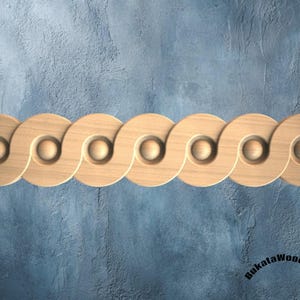 May include: A horizontal wooden molding strip featuring a repeating pattern of interlocking circular shapes with a central concave indentation. The light-colored wood grain is visible across the continuous, wave-like design. Text reads Bukatawoodwork.