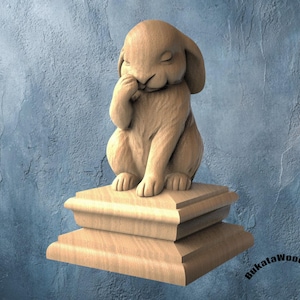 May include: A wooden sculpture of a rabbit sitting on a tiered base. The rabbit is light brown, with its eyes closed and a paw touching its face. The base is also light brown and has a layered design. The background is a textured blue.