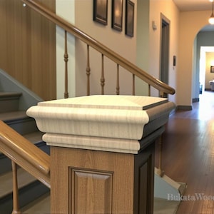 May include: A wooden newel post with a decorative top and a paneled base. The post is part of a staircase with a wooden handrail and balusters. The interior features a hallway with a hardwood floor and a view of a living room.