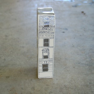 May include: A white ceramic figurine shaped like a tall building with three windows and a black and white design.