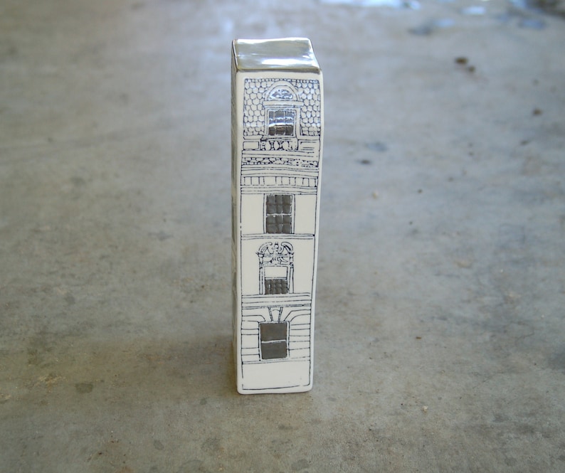 May include: A white ceramic figurine shaped like a tall building with three windows and a black and white design.