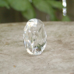 May include: A clear glass oval-shaped pendant with a carved design. The pendant is smooth and polished.
