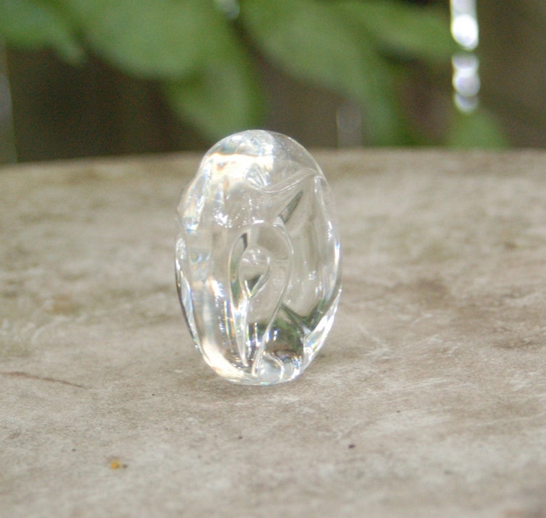 May include: A clear glass oval-shaped pendant with a carved design. The pendant is smooth and polished.