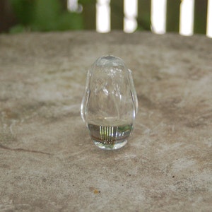 May include: A clear glass bottle stopper with a rounded shape and a textured surface.