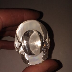 May include: Clear glass paperweight with a rounded, organic shape. The paperweight has a smooth, polished surface and a slight iridescent sheen.