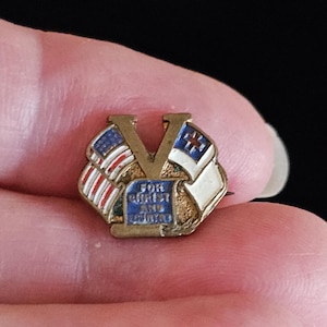 May include: A gold-tone metal lapel pin featuring a large letter V centred behind two crossed flags. The left flag is the American flag, and the right flag is a white Christian flag with a blue cross. A blue rectangular plaque reads FOR CHRIST AND COUNTRY.