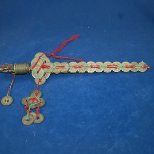 May include: A decorative sword made of a series of linked Chinese coins, tied together with red and green string. The sword has a metal handle and a tassel of coins hanging from the bottom.