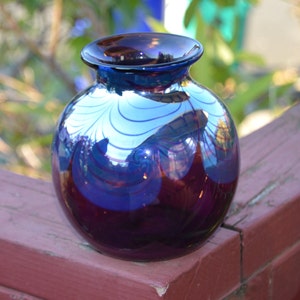 May include: A round, iridescent glass vase with a blue and purple swirl pattern. The vase is sitting on a wooden surface.