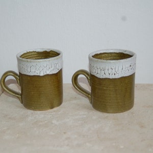 Puede incluir: Dos tazas de cerámica con un borde blanco y un esmalte verde. Las tazas tienen un aspecto rústico y hecho a mano.