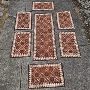 May include: A set of seven rectangular fabric mats featuring a brown and white batik pattern with geometric floral motifs and a repeating leaf-like border. The collection includes one long runner and six smaller matching rectangular placemats.