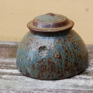 May include: A ceramic jar with a lid, featuring a mottled blue and brown glaze. The jar has a round body and a slightly flared rim.