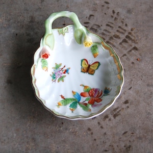 May include: A white porcelain dish with a green handle and a butterfly design. The dish is decorated with flowers and leaves in shades of red, yellow, green, and blue.