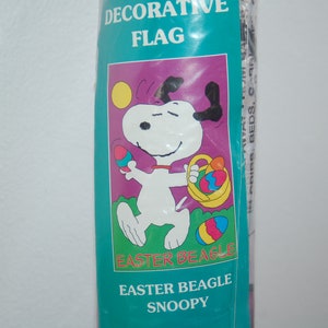 May include: A decorative flag featuring Snoopy, the Peanuts character, holding a basket of Easter eggs. The flag is purple with a yellow sun and green grass. The text "Easter Beagle Snoopy" is printed on the flag.