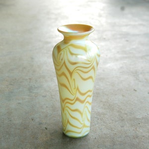 May include: A white and gold iridescent glass vase with a swirling pattern. The vase is tall and slender with a rounded base.