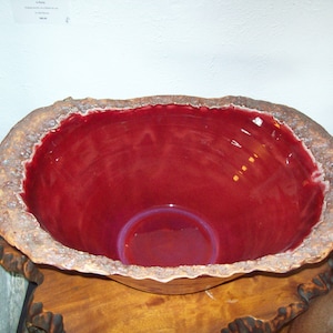 May include: A large, red ceramic bowl with a rough, textured exterior. The bowl has a deep, rounded interior and a wide, flared rim.