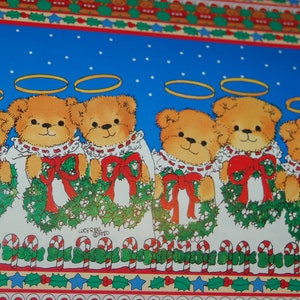 May include: A blue and white Christmas wrapping paper with a repeating pattern of teddy bears wearing halos and holding wreaths. The bears are wearing white dresses with red bows. The paper has a border of holly, candy canes, and stars.