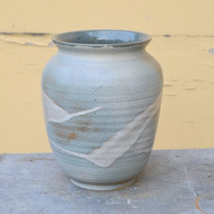 Puede incluir: Un jarrón de cerámica azul claro con esmalte blanco y marrón, con un diseño ondulado.