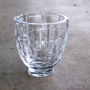 May include: A clear glass vase with a geometric pattern. The vase has a wide mouth and a round base.