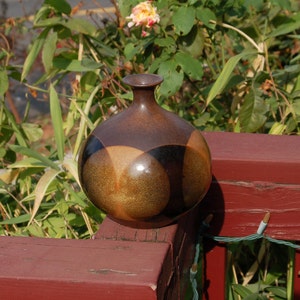 Op de afbeelding: Een bruine en zwarte keramische vaas met een geometrisch ontwerp. De vaas heeft een ronde vorm en een glanzende afwerking.