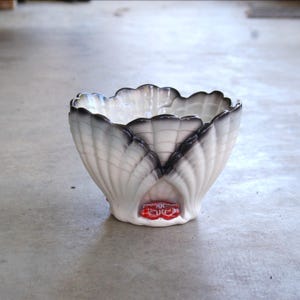 May include: A white ceramic bowl with a scalloped edge and a black and grey design. The bowl has a red and white design on the bottom.