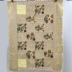 May include: A beige quilt with a repeating pattern of brown and yellow floral motifs. The quilt is made up of squares with a yellow background and a brown floral design. The quilt is edged with a brown and yellow trim.