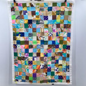 May include: A colorful patchwork quilt with a white background and a variety of fabrics in shades of blue, green, pink, orange, and brown. The quilt is made up of small squares, each with a different pattern.