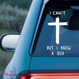 May include: White decal on a car window featuring a cross and the text "I CAN'T BUT I KNOW A GUY." The decal is applied to the rear window of a teal car, with a side mirror visible.