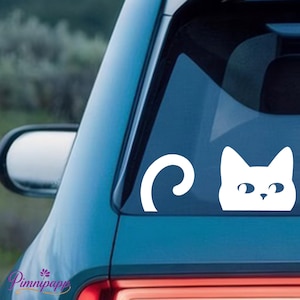 May include: White vinyl decal of a cat's head and tail, designed to be applied to a car window. The cat's head is a simple, stylized design with two ears and eyes. The tail is a curved shape.
