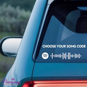 May include: White vinyl decal applied to a car window. The decal features the Spotify logo, a barcode-like graphic, and the text "CHOOSE YOUR SONG CODE". The car is teal, and the background is blurred.