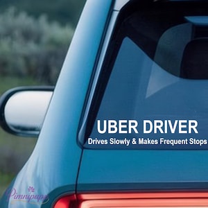 Peut inclure: Autocollant blanc sur une vitre de voiture turquoise avec l'inscription "UBER DRIVER" en gras, et le texte "Drives Slowly & Makes Frequent Stops" en dessous. Le rétroviseur de la voiture est visible.